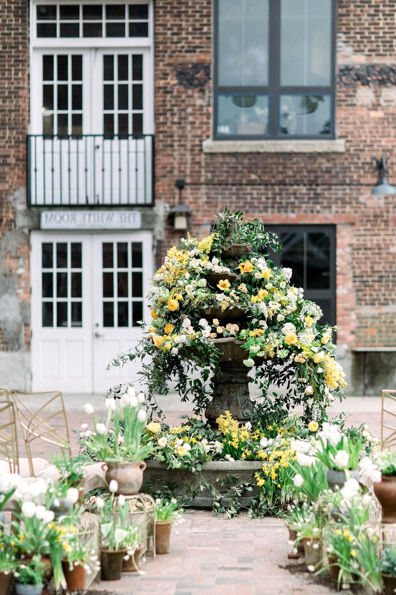 courtyard wedding ceremony with potted plant aisle markers and a floral fountain backdrop
