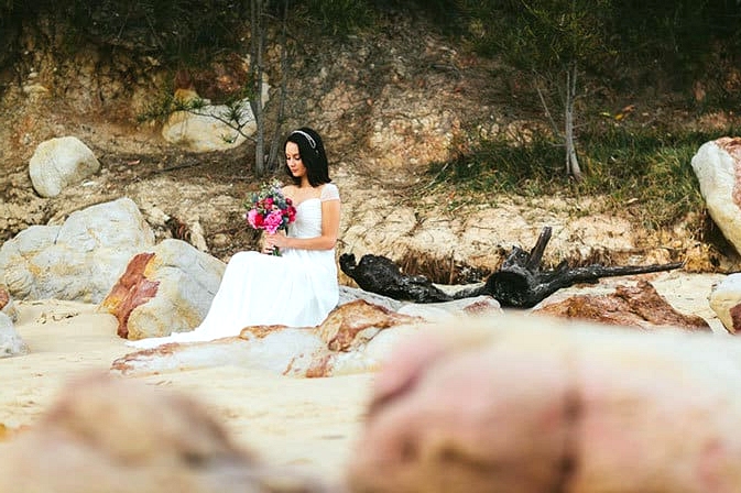 Bride sitting on beach with bright bouquet