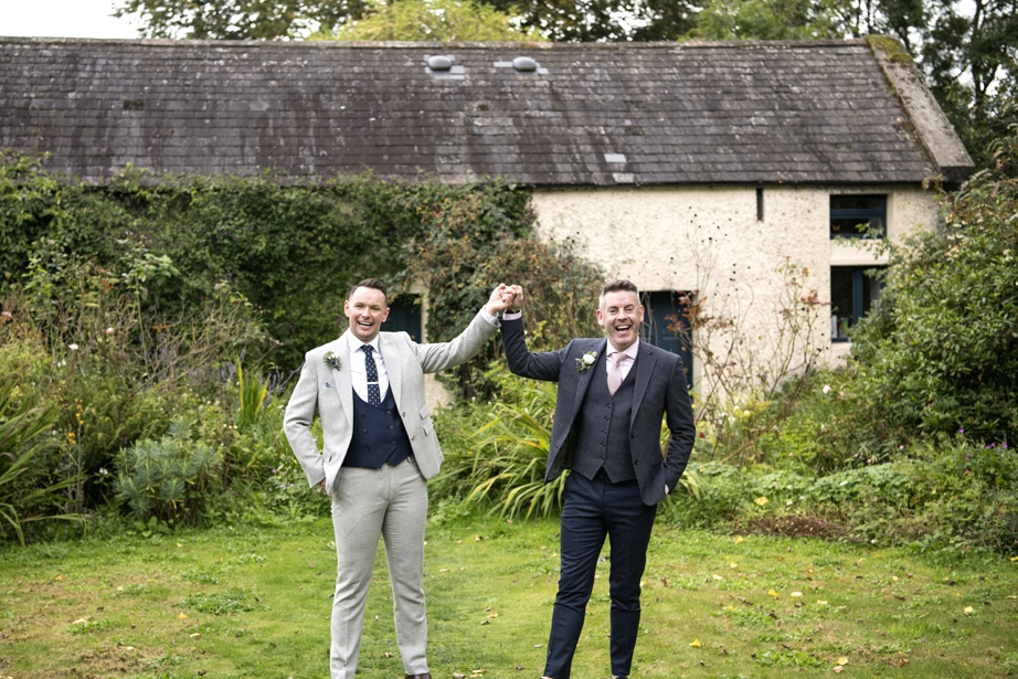 Eoin & Darran Real Wedding hand in hand exterior barn green setting smiling grooms