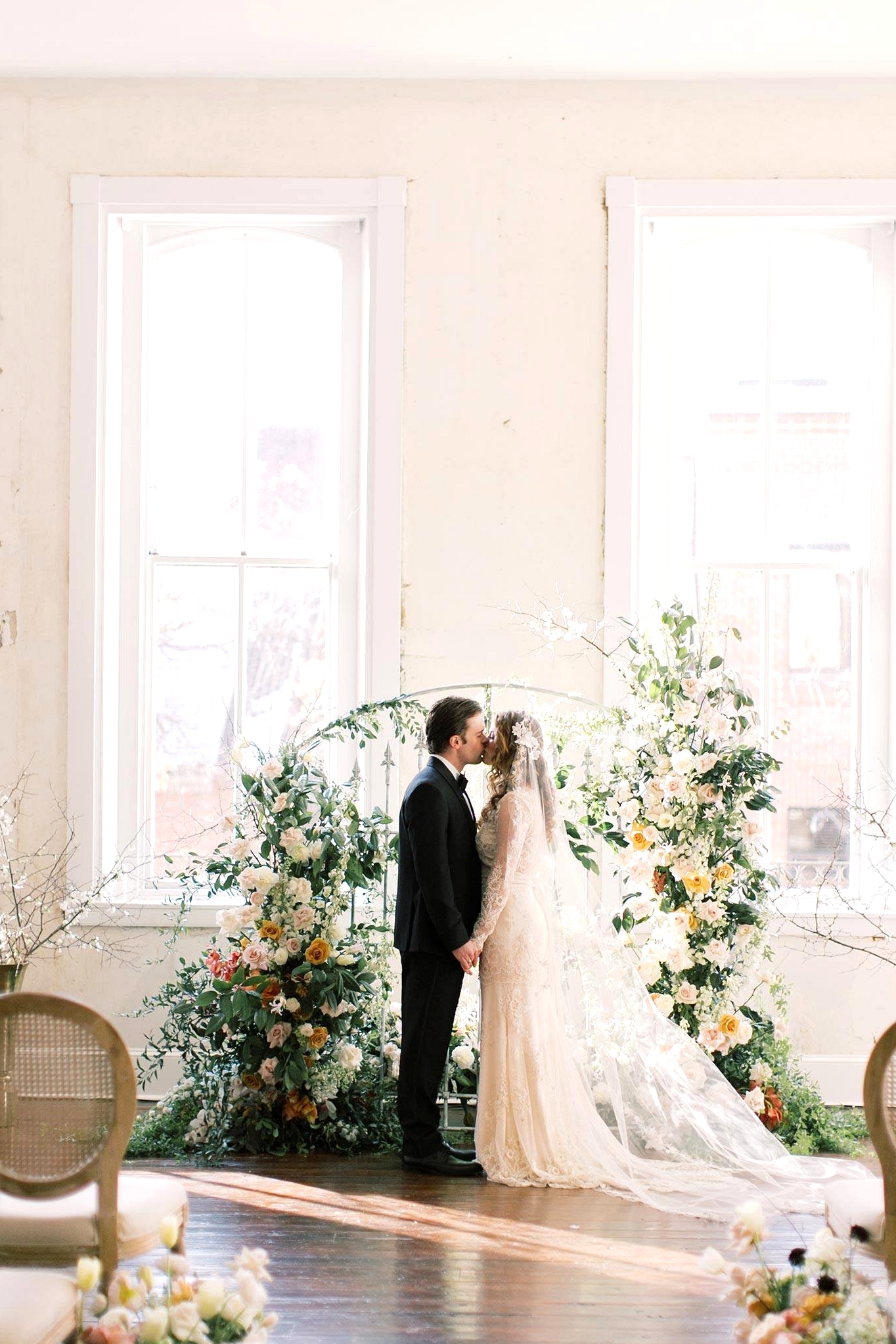 Old World wedding backdrop with a floral iron gate and bride and groom kissing