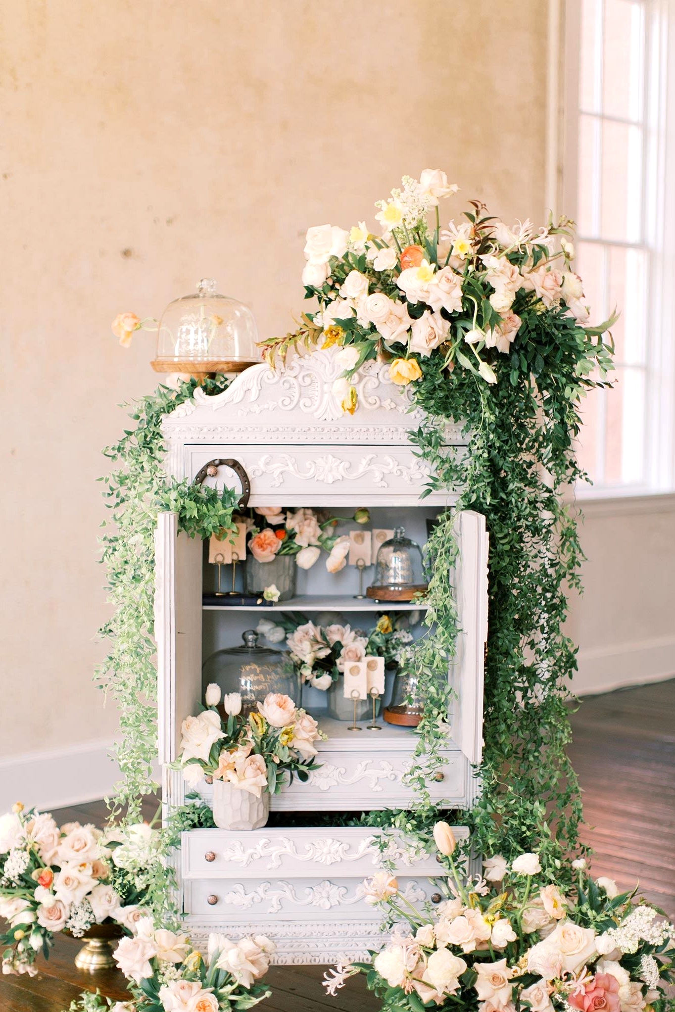 calligraphed cloche seating chart in a shabby chic bookshelf with greenery and fresh flowers