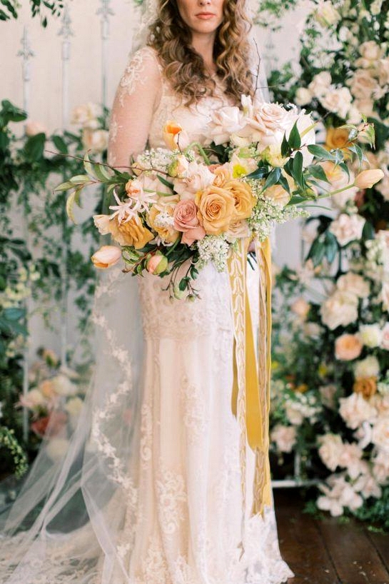 lush floral gate wedding backdrop with bride in a vintage-inspired wedding dress holding a yellow and white spring bridal bouquet