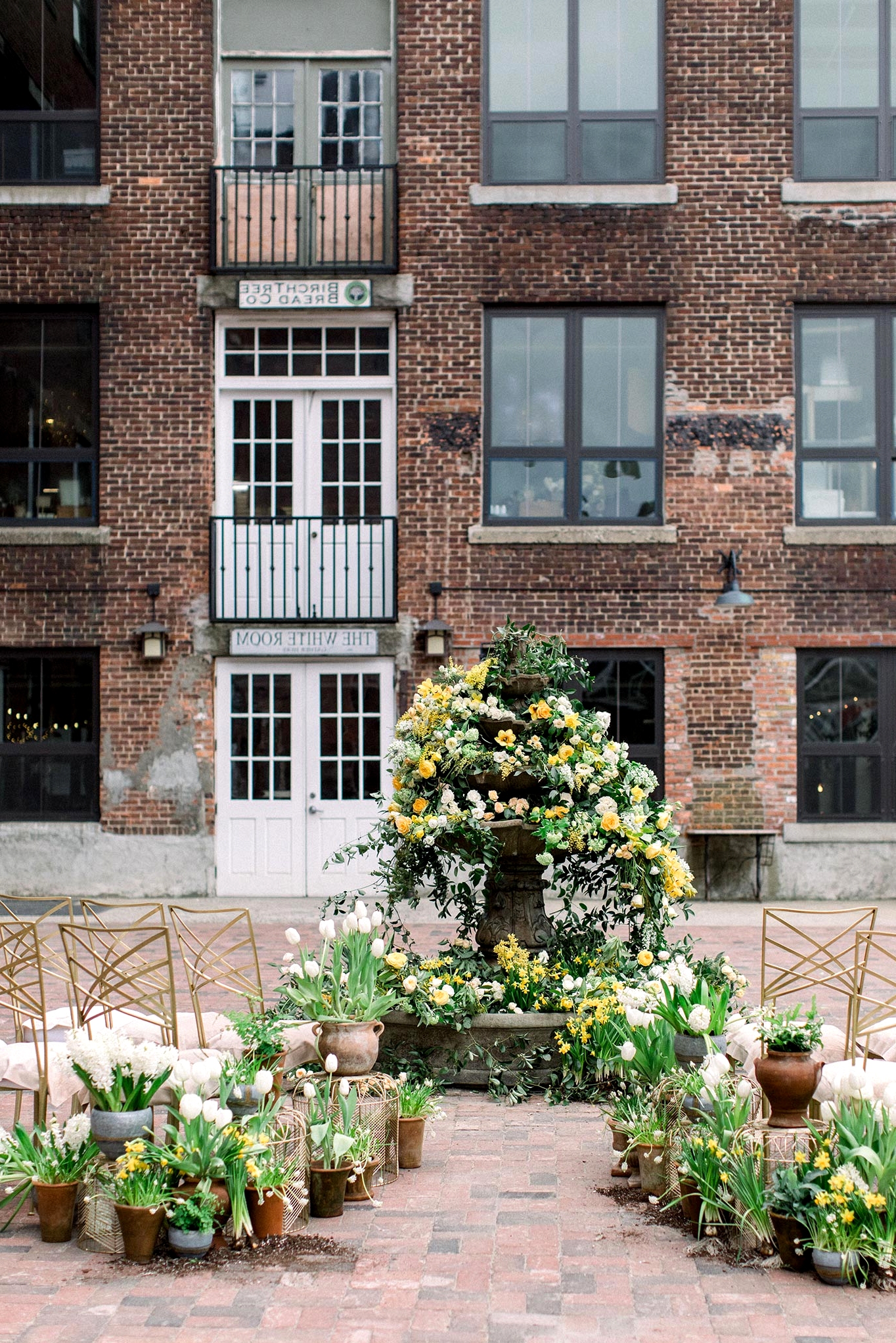 courtyard wedding ceremony with potted plant aisle markers and a floral fountain backdrop