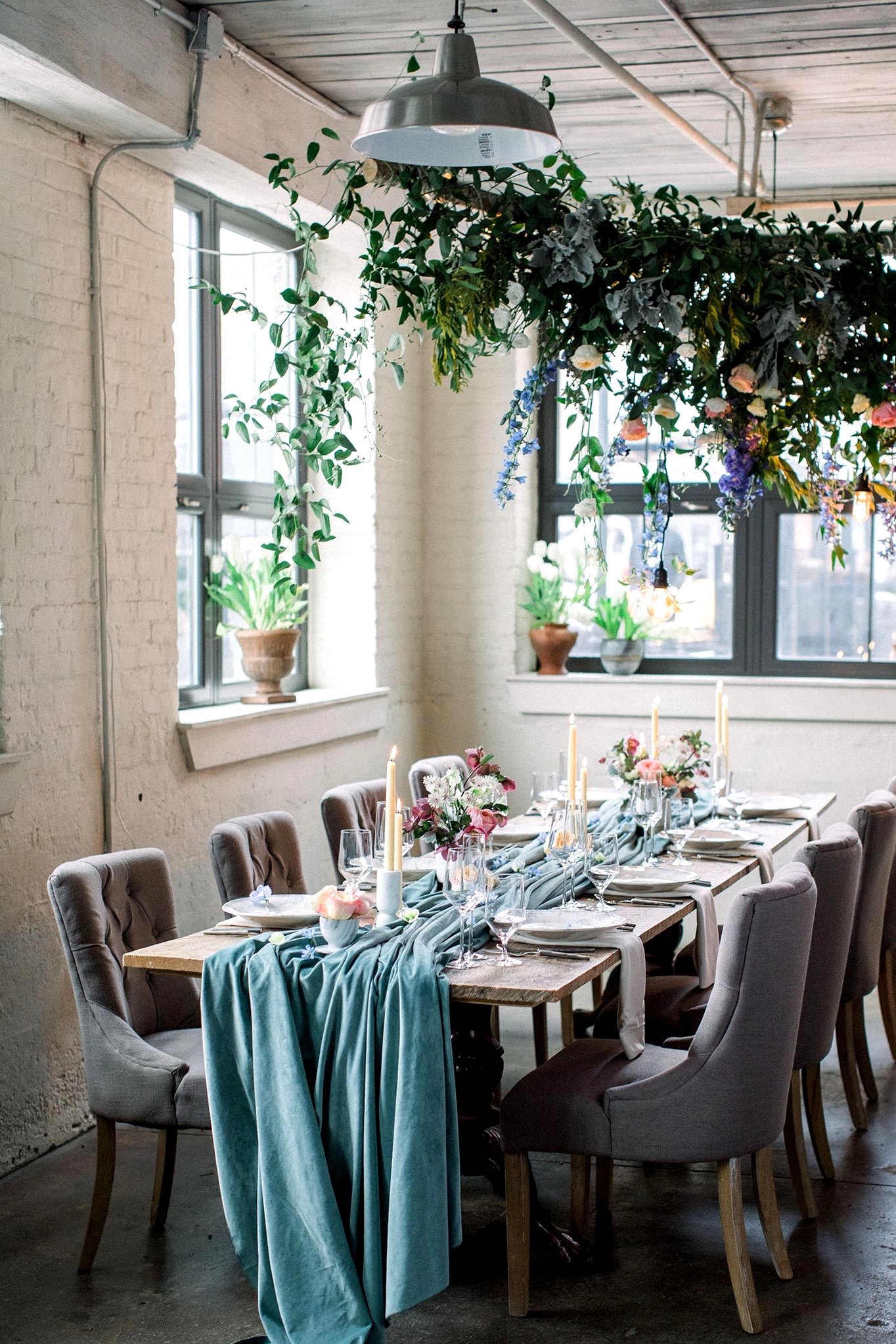 cozy white brick wedding reception with potted plants, a floral canopy and velvet teal table runner