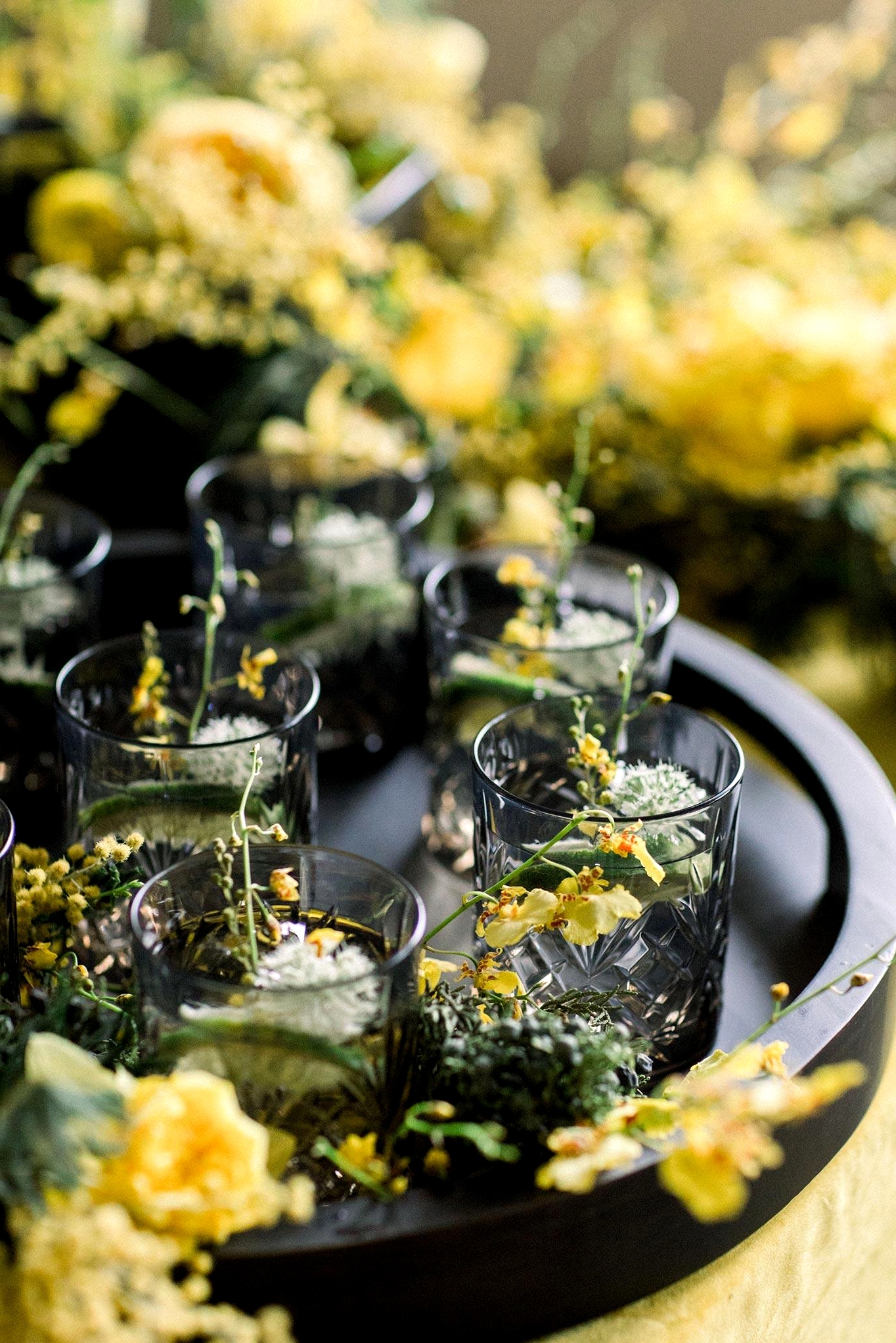 black crystal cut glassware with botanical cocktails on a matte black serving tray with yellow flower accents