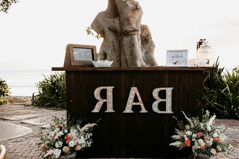 Maui wedding reception with a rustic chic bar and marquee light bar signage 