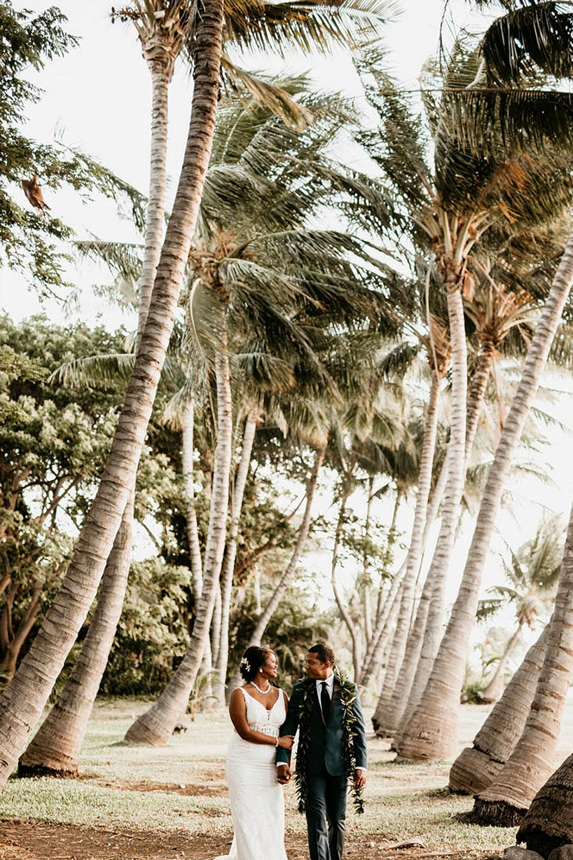 Maui wedding couple portraits beneath palm trees with bride in a v-neck wedding dress and groom with a traditional Hawaiian lei