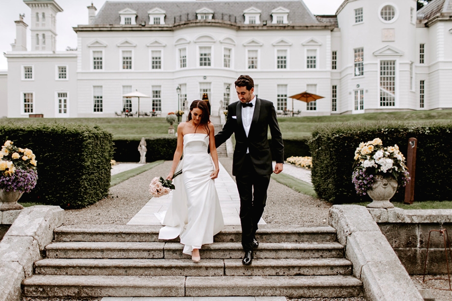 Exterior bride and groom walking down hotel steps flowers holding pink roses bouquet